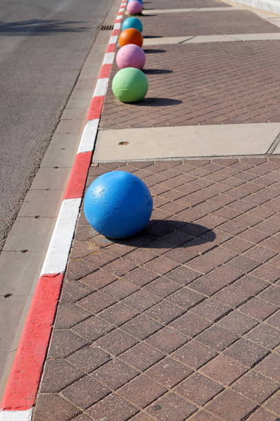 bolas de concreto multi-coloridas encontram-se na calçada da cidade e servem como uma barreira a partir da pista
  - Foto, Imagem