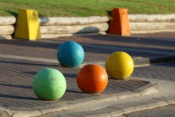 разноцветные бетонные шары лежат на тротуаре в городе и служат барьером от проезжей части
  - Фото, изображение