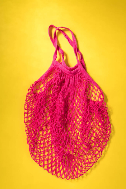 Επαναχρησιμοποιήσιμο φούξια τσάντα με δίχτυ σε κίτρινο φόντο. Μηδενική σπατάλη, πλαστική ιδέα χωρίς πλαστικά, Eco ευγενέστατο. - Φωτογραφία, εικόνα