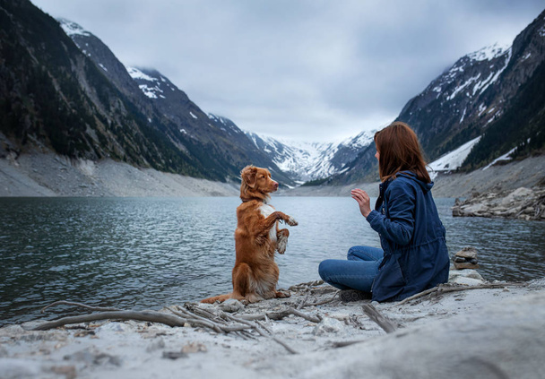 woman with a toller dog at the mountains lake. Traveling with a pet. Nova Scotia Duck Tolling Retriever - Photo, Image