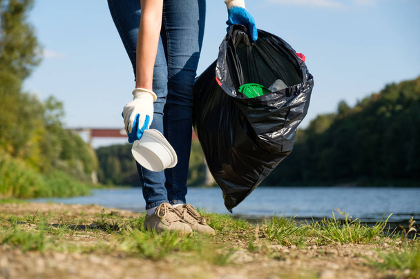 Mulher voluntária recolhendo lixo plástico na costa do rio. Conceito de ambiente de limpeza
 - Foto, Imagem