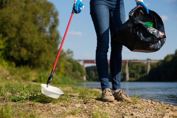 Volunteer woman picking up plastic litter on coast of the river. Cleaning environment concept - Photo, Image