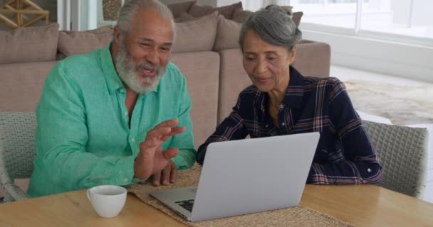 Front view close up of a smiling mature mixed race couple using a laptop computer and talking at home - Materiaali, video