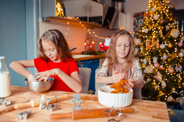 Kleine Mädchen basteln Weihnachts-Lebkuchenhaus am Kamin im geschmückten Wohnzimmer. - Foto, Bild