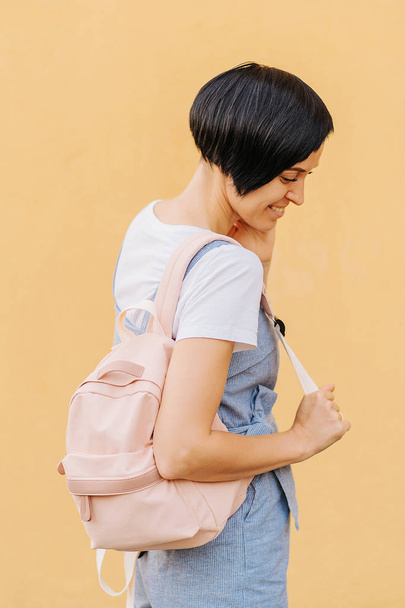 Portrait of young woman with a backpack on pale yellow wall. - Foto, imagen