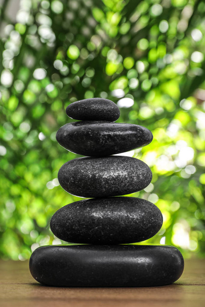 Table with stack of stones and blurred green leaves on background. Zen concept - Photo, Image
