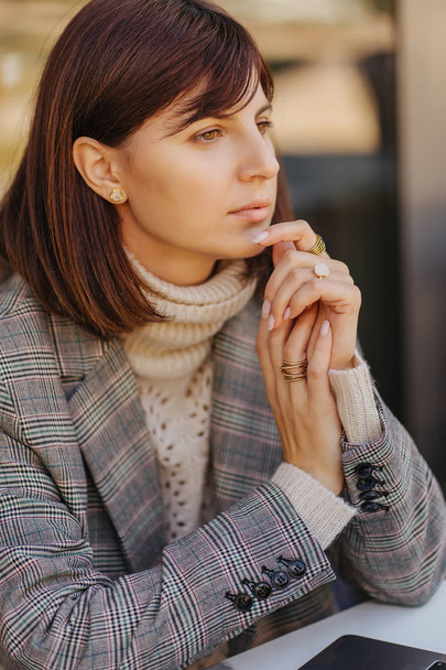 Porträt einer jungen Frau in warmem Pullover und Blazer in einem Café auf der Terrasse  - Foto, Bild