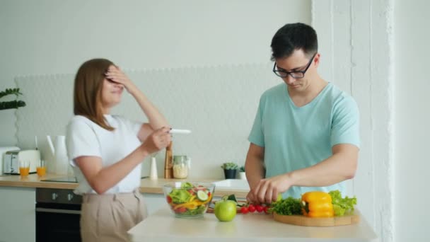 marido hombre cocina comida en la cocina cuando feliz chica trayendo prueba de embarazo
 - Metraje, vídeo