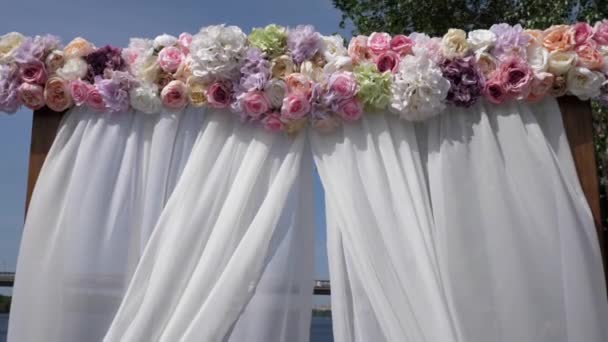 Bruiloft boog van witte stof en een houten basis aan de oevers van de rivier de Dnjepr op de achtergrond van de brug. Huwelijksceremonie. - Video