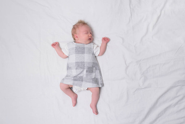 Dormir niña recién nacida en un vestido en una sábana blanca. Vista superior. Espacio para texto
 - Foto, imagen