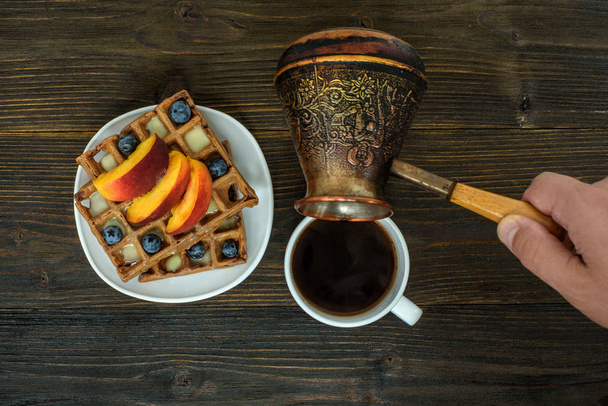 Belgian waffles with fruit and berries. Male hand pours coffee from a coffee pot. Top view - Photo, Image
