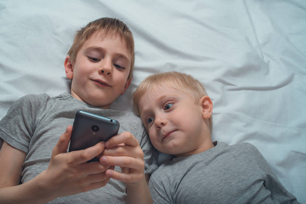 Two boys are lying in bed with a smartphone. Gadget Leisure - Photo, image