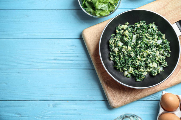 Flat lay composition of tasty cooked spinach and space for text on light blue wooden table. Healthy food - Φωτογραφία, εικόνα
