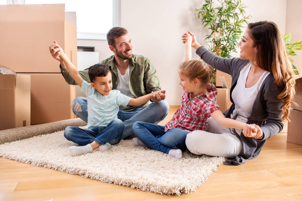 Счастливая семья сидит на полу своей новой квартиры
  - Фото, изображение