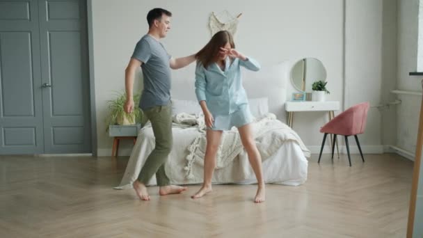 Slow motion of happy couple girl and guy dancing in bedroom laughing having fun - Metraje, vídeo