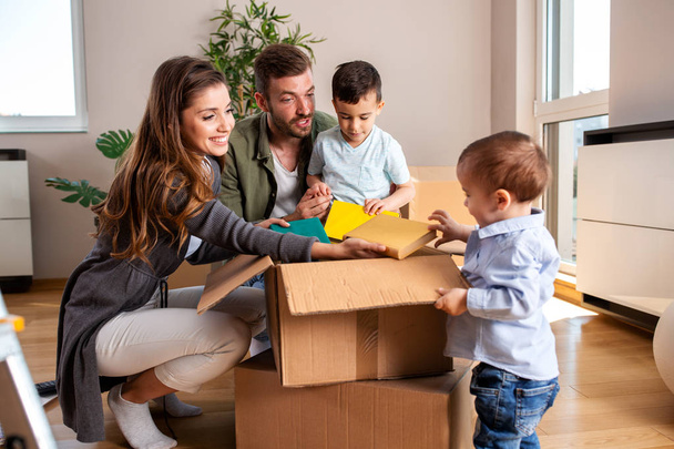 Young couple unpacking boxes with their two sons - Foto, imagen