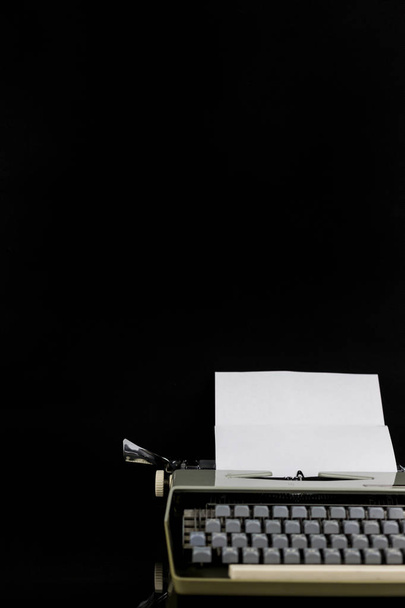 Maszyna do pisania na stole na czarnym tle z białym papierze z pustą przestrzenią. Miejsce pracy pisarza lub autora. Koncepcja pomysłu. - Zdjęcie, obraz