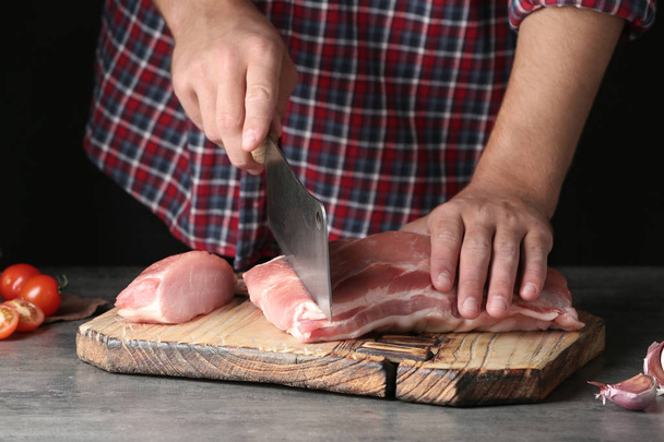 Man cutting fresh raw meat on table against dark background, closeup - 写真・画像