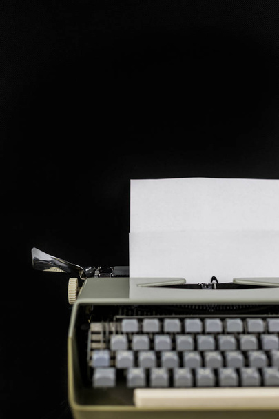 Typewriter op de tafel op een zwarte achtergrond met wit papier met lege ruimte. Werkplek van de schrijver of auteur. Idee concept. - Foto, afbeelding
