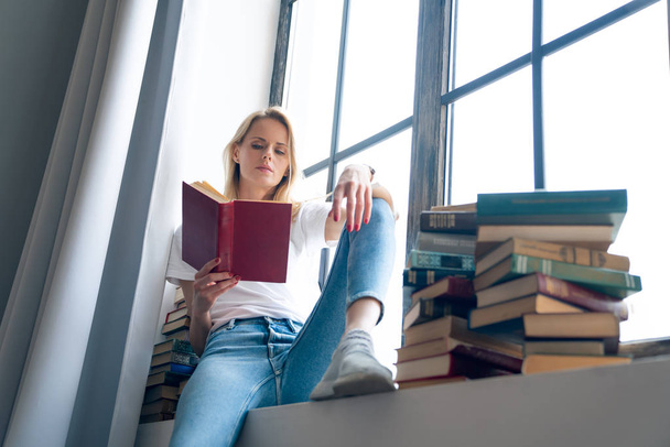 Düşünceli depresif, yalnız genç kadın fikir ve favori yazarın yeni bestseller arsa üzerinde kafa yoruyor şık coworking alanda rahat pencere üzerinde dinlenme. - Fotoğraf, Görsel