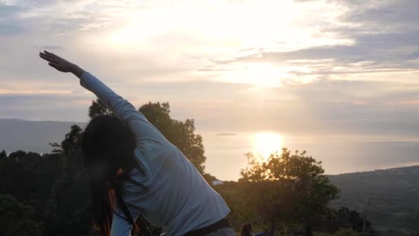 Widok z tyłu młodej kobiety robi rozgrzewkę ćwiczenia w górach o wschodzie słońca. - Materiał filmowy, wideo