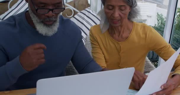 Front view close up of a mature mixed race man using a laptop computer and a mature mixed race woman holding a document and discussing at home - Filmagem, Vídeo