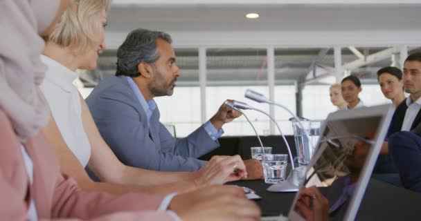 Side view close up of three business delegates, a young Asian woman wearing a hijab, a middle aged blonde Caucasian woman and a middle aged mixed race man with a beard sitting in a row at a table with microphones in front of them  - Metraje, vídeo