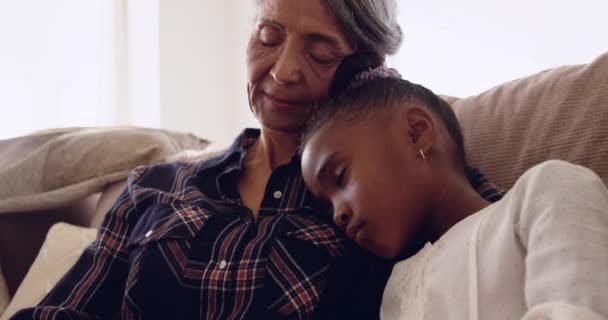 Front view close up of a mature mixed race woman sleeping with her young granddaughter sitting on a sofa at home - Séquence, vidéo
