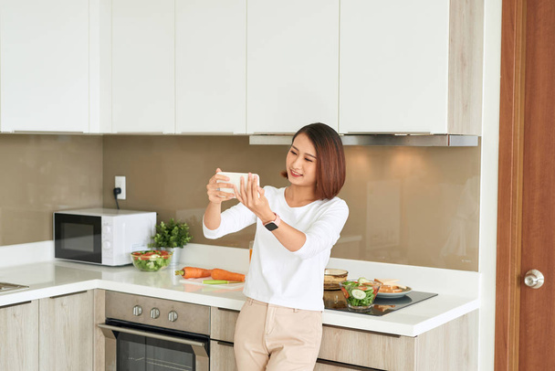 Portrait of smiling asian housewife making selfie in domestic kitchen - Φωτογραφία, εικόνα