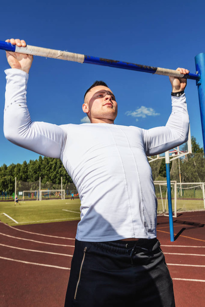 Sport, street workout concept - athlete doing pull ups on the horizontal bar outdoors. - Valokuva, kuva