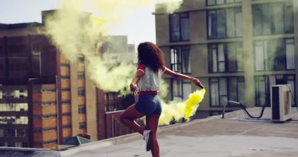 Back view of a hip young mixed race woman walking and using smoke grenade on an urban rooftop, with buildings in the background - Séquence, vidéo