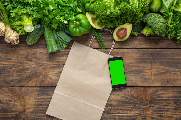 Smartphone with blank screen for your text message or design with green green vegetables on wooden background - Fotografie, Obrázek