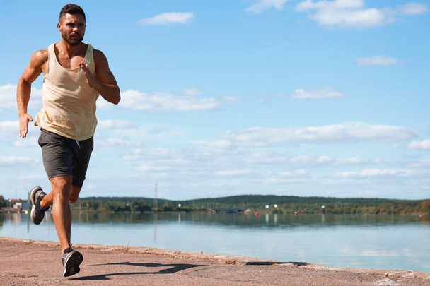 Sterke sport man joggen tijdens het sporten uit in de buurt van de stad Riverfront - Foto, afbeelding