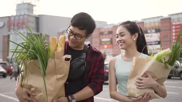 Good-looking smiling vietnamese couple going from the supermarket with bags full of various food - Filmati, video