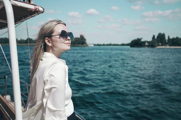 Приваблива усміхнена дівчина в білій сорочці і сонцезахисних окулярах на яхті. Концепція яхтингу або круїзу на морі або річці
. - Фото, зображення