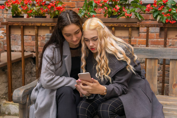 δύο φιλενάδες που συζητούν κάτι ενώ αναζητούν ένα smartp - Φωτογραφία, εικόνα