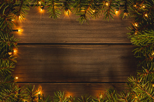 Christmas frame with lights and fir branches on wooden background top view and copy space image - Photo, Image