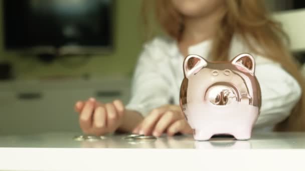Dziewczyna przedszkolaka stawia pieniądze w Skarbonka różowy świnia - Materiał filmowy, wideo