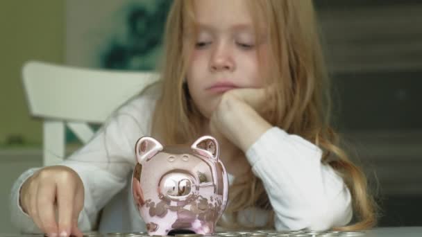 女の子の未就学児は、貯金箱ピンクの豚にお金を入れます - 映像、動画