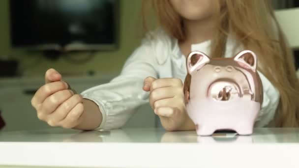 Dziewczyna przedszkolaka stawia pieniądze w Skarbonka różowy świnia - Materiał filmowy, wideo