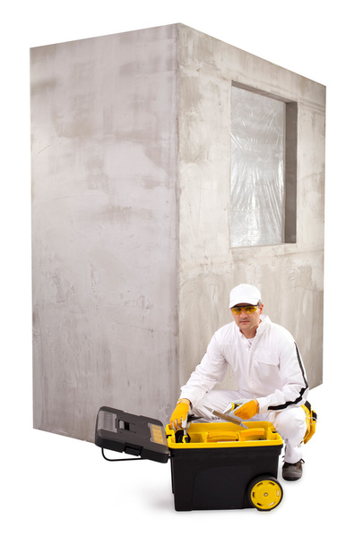 Rakennustyöntekijä, jolla on valkoiset haalarit, musta työkalupakki ja sementti
 - Valokuva, kuva