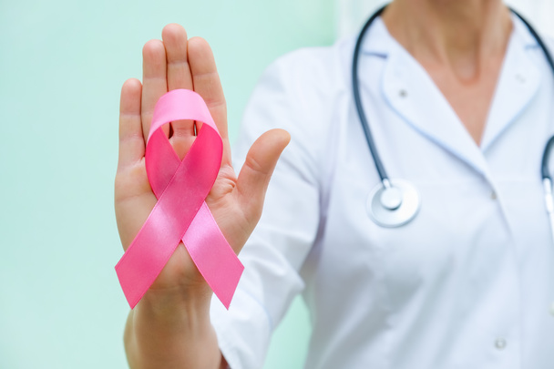 Roze lint voor borstkanker bewustzijn in de hand van de arts, vrouwen borsttumor ziekte campagne. - Foto, afbeelding