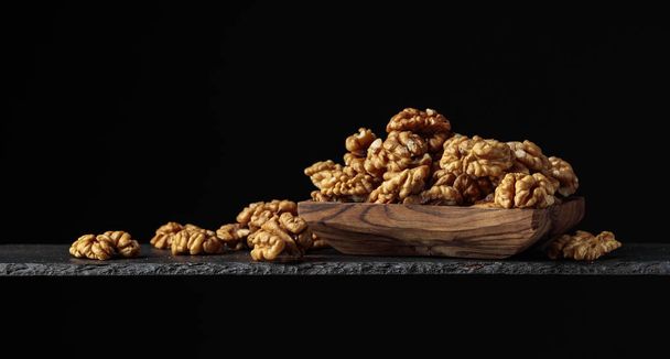 Walnuts in wooden dish on a black background.  - Photo, Image
