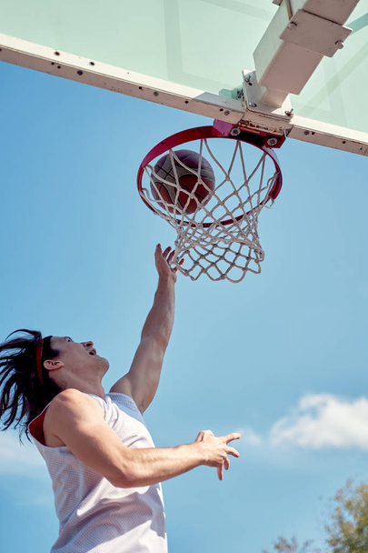 Image of athlete man throwing ball into basketball hoop on sports field on street on summer day. - Foto, Imagem