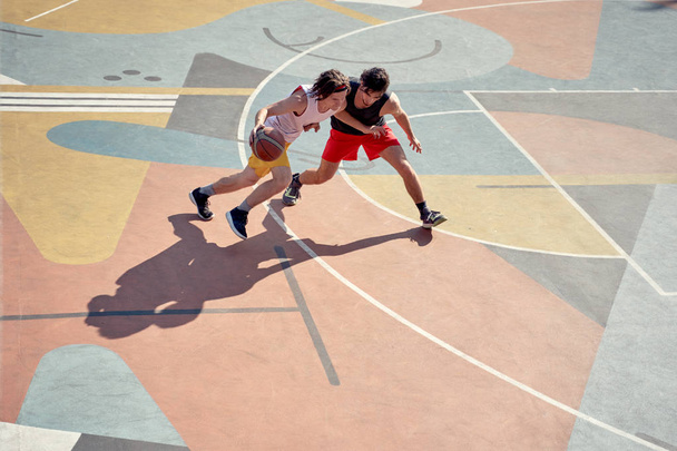 Top view photo of two young athletes men playing basketball on playground in morning. - 写真・画像