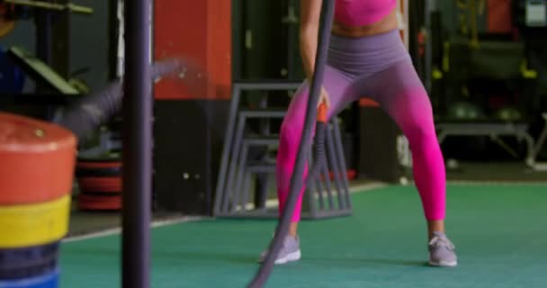 Front view of a young Caucasian woman exercising in a gym, using battle ropes - Felvétel, videó