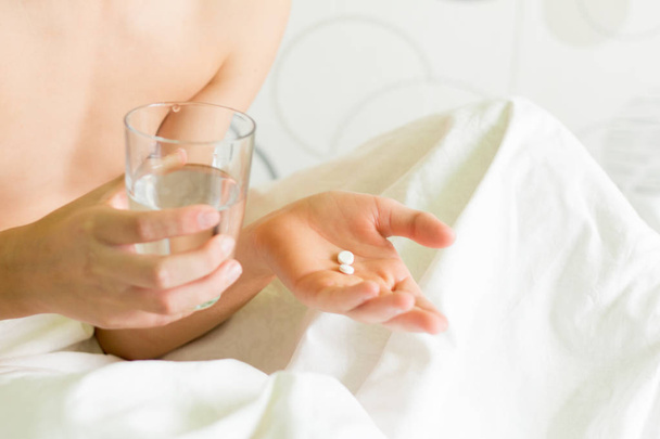 Una persona enferma sostiene un vaso de agua y pilas.Toma medicamentos para la enfermedad
 - Foto, Imagen
