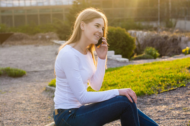 Young beautiful woman talking by mobile phone in spring at sunse - Foto, Imagen