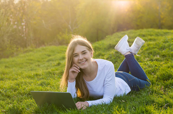 Young beautiful woman student with a laptop lies on the grass in - Φωτογραφία, εικόνα