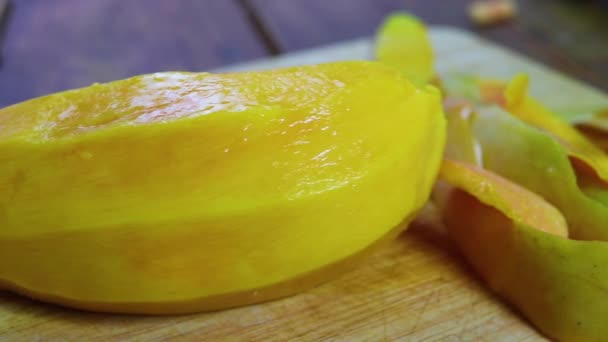 Fiatal nő tisztítja és csökkenti mangó. Lány peeling mangó és tartsa a kezében, a homárpartyn késsel. peeling érett mangó, érett mangó és a nyesedék kés használt héj ez a háttérben. - Felvétel, videó